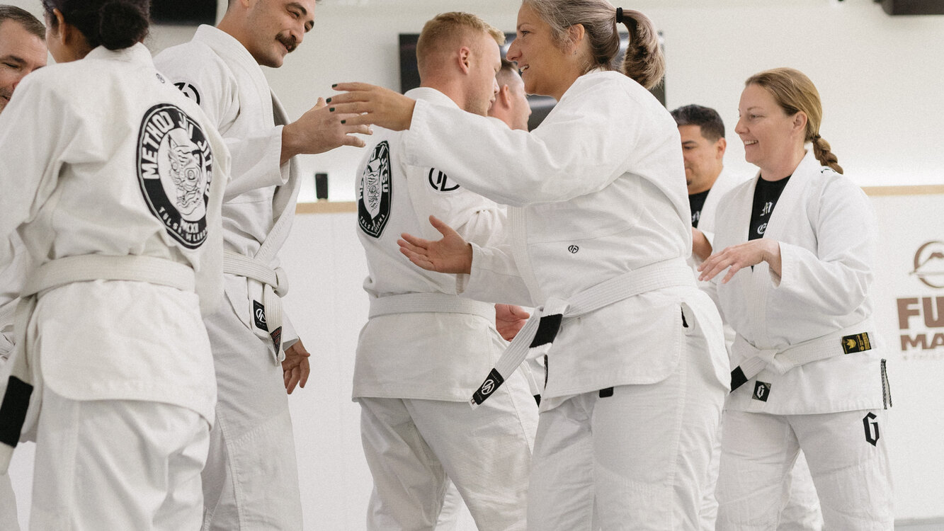 Smiling adult white belts in Method Jiu-Jitsu gis high-fiving and greeting training partners at the end of a BJJ class in South Tulsa