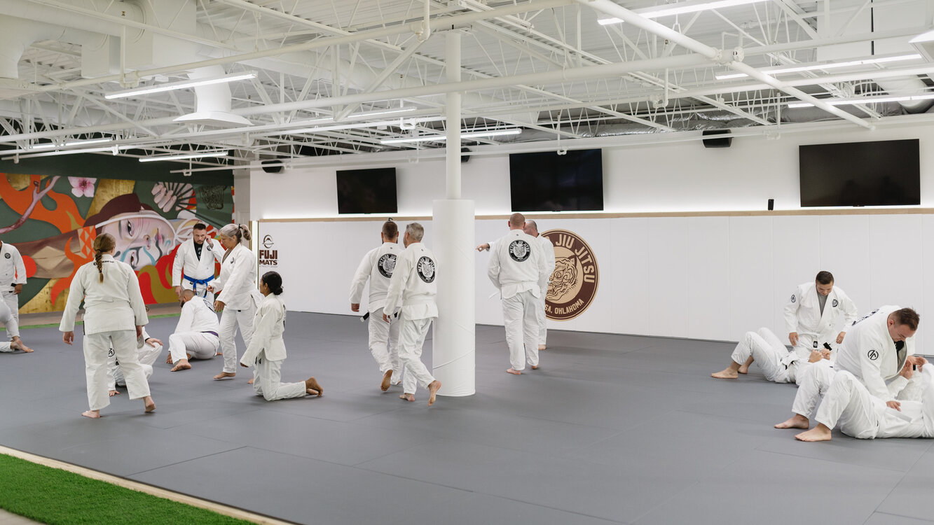 Students in white gis moving across the mats and starting partner drills during a gi class at Method Jiu-Jitsu in Tulsa