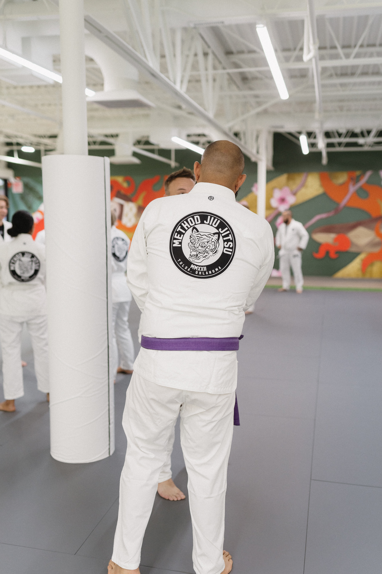 Purple-belt jiu-jitsu practitioner in a white Method Jiu-Jitsu gi training with teammates on the Tulsa mats